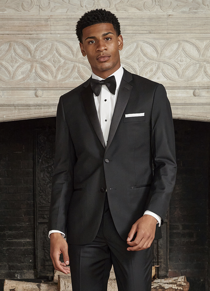 A Man in a black tuxedo stands in front of a fire place