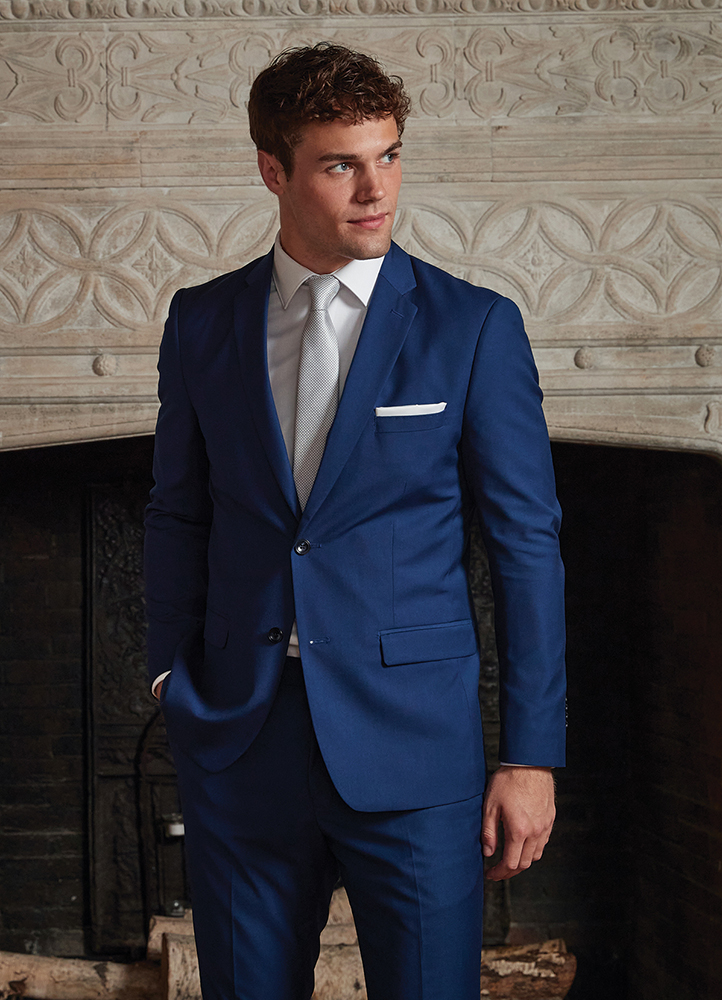 a handsome man stands in a suit in front of a fire place.
