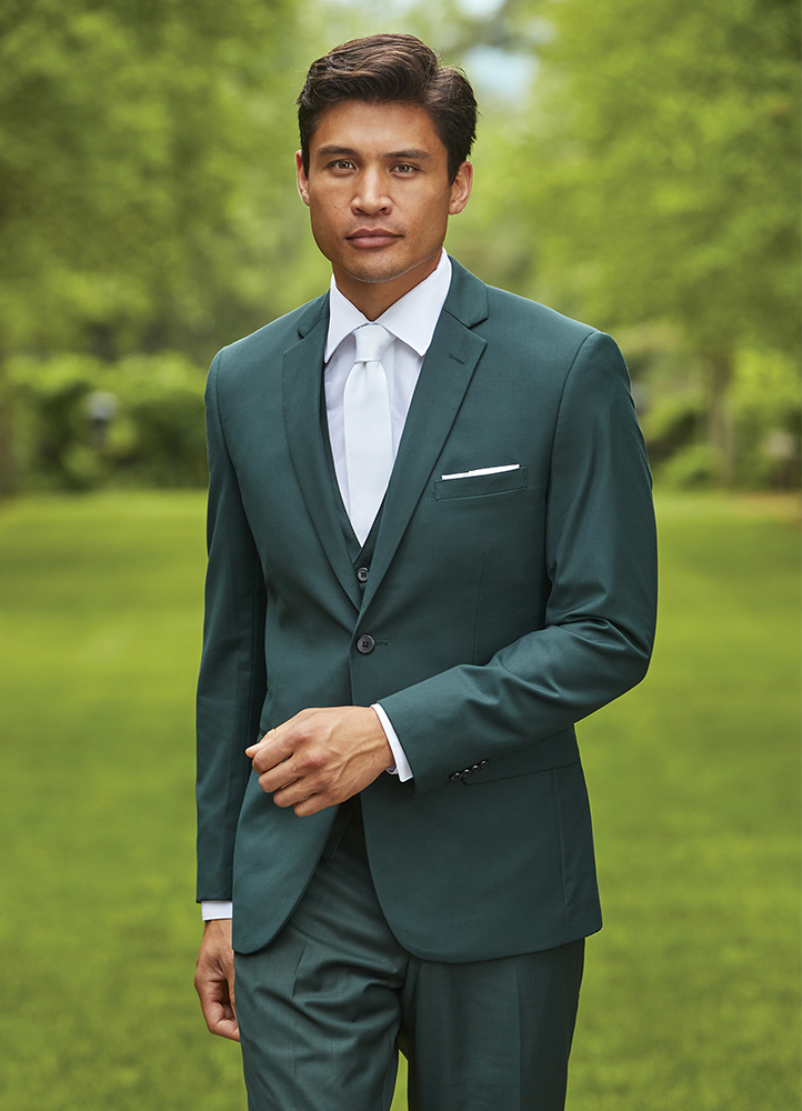 A man in a green suit stands in front of a very green courtyard.
